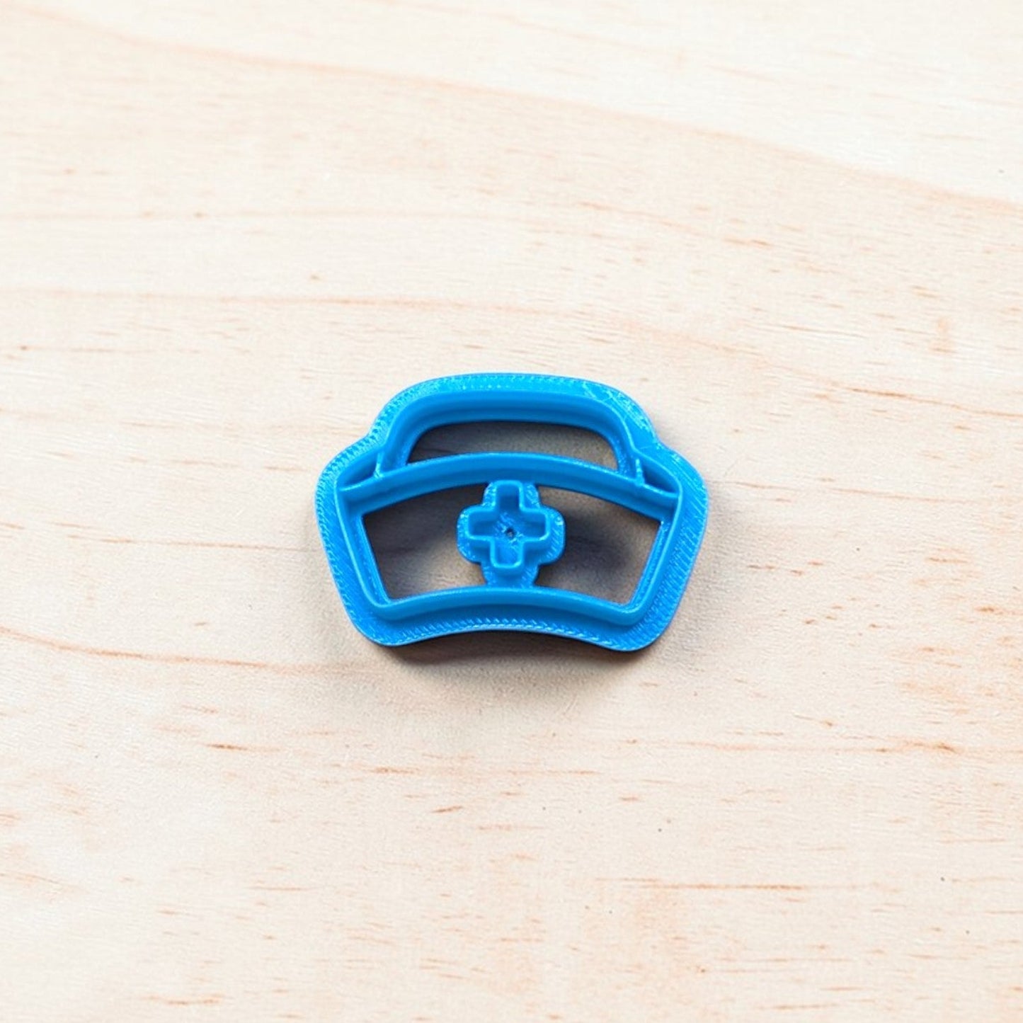 Blue cookie cutter shaped like a nurse cap on a light wooden surface