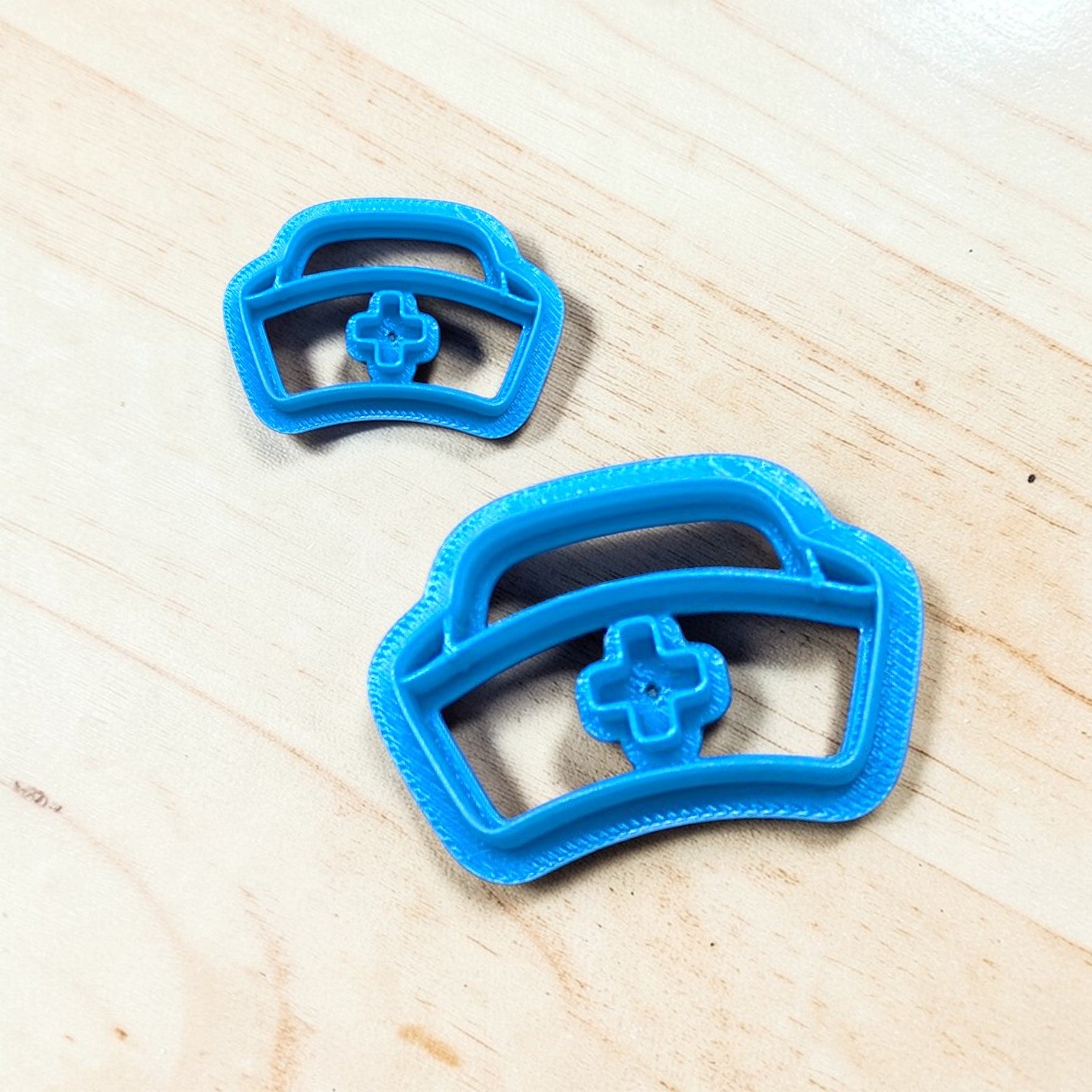 Two blue cookie cutters shaped like nurse caps on a wooden surface