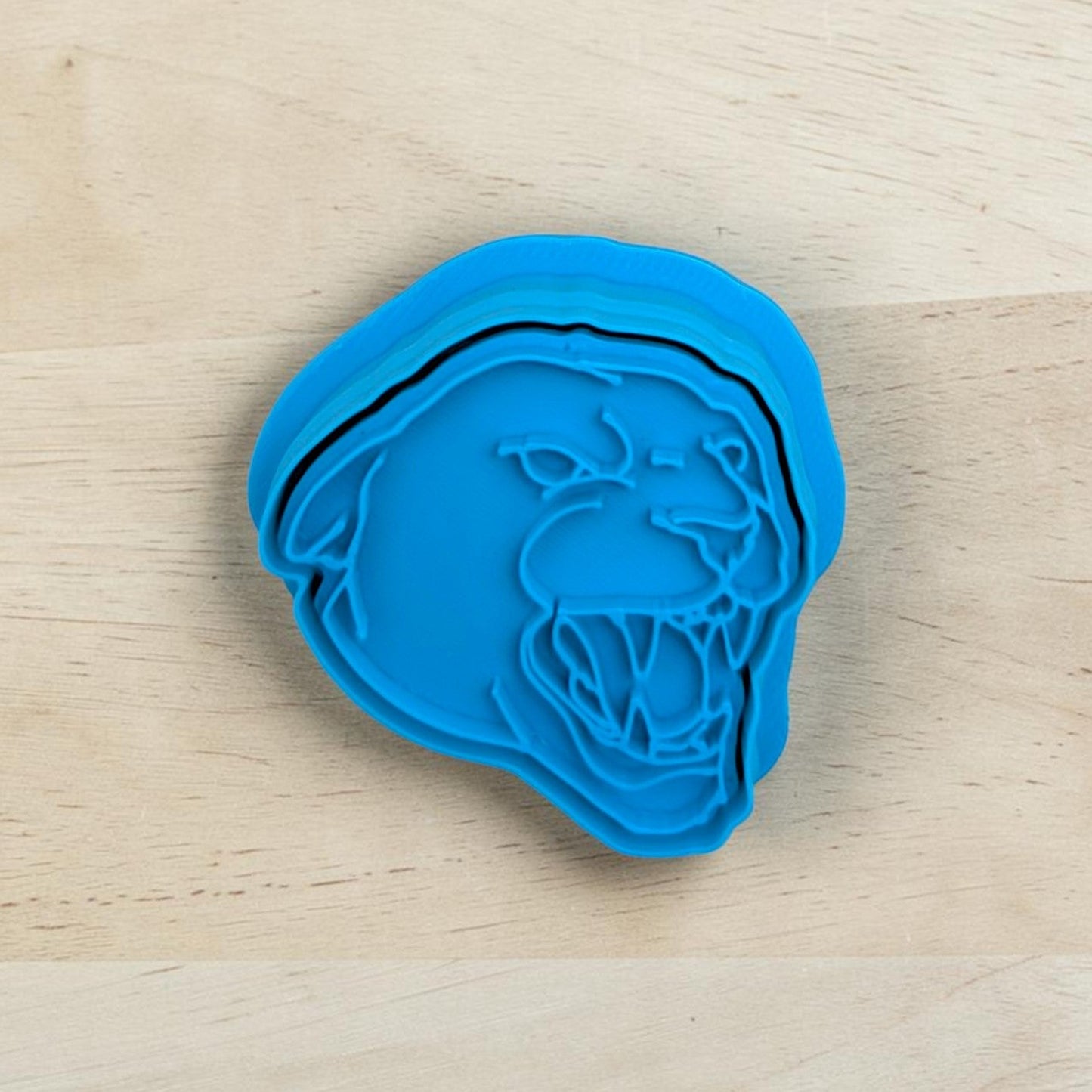 A bright blue plastic cookie cutter with a snarling panther design, placed on a light-colored wooden surface.