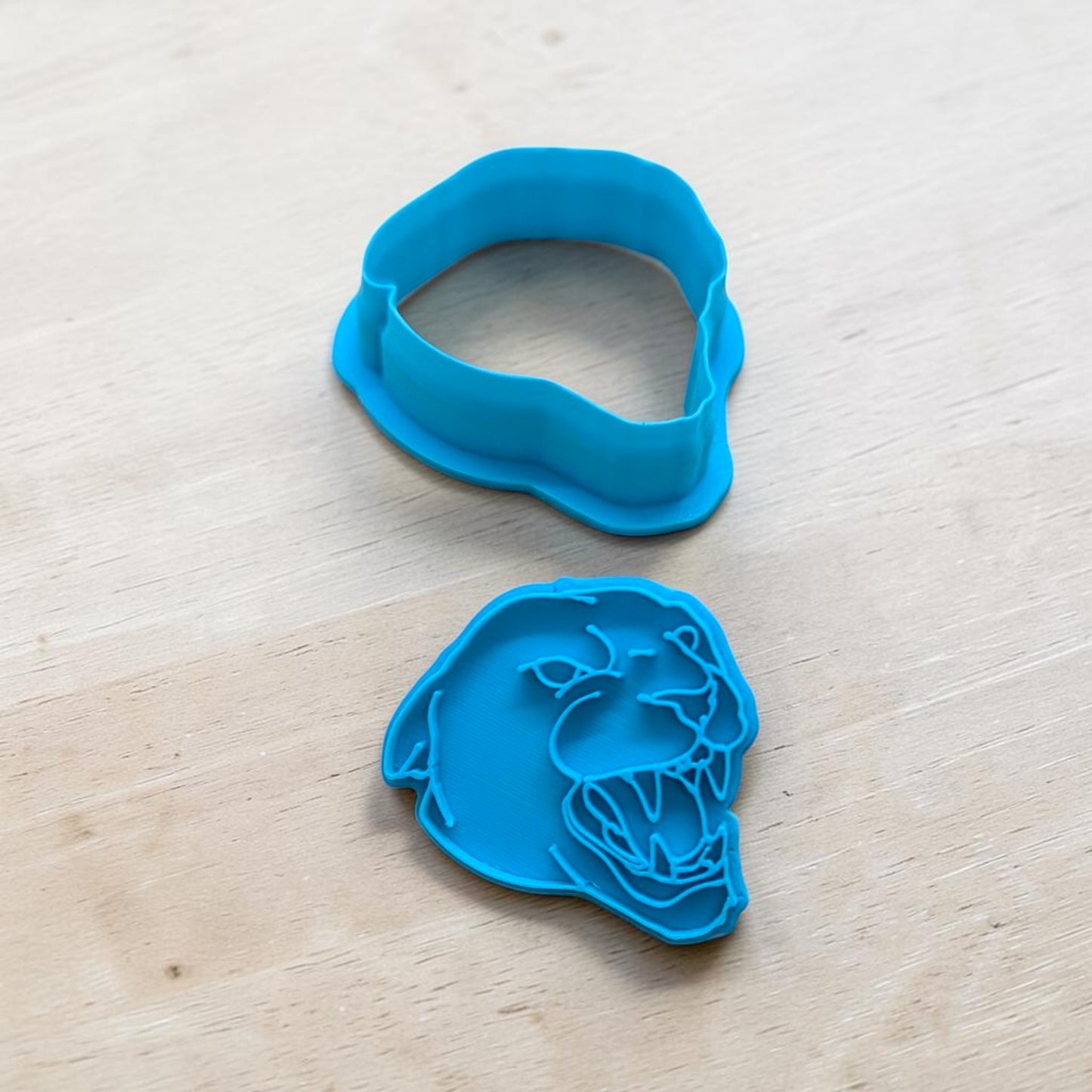 A bright blue plastic cookie cutter and matching cutout template shaped like a snarling panther, displayed on a light wood surface.