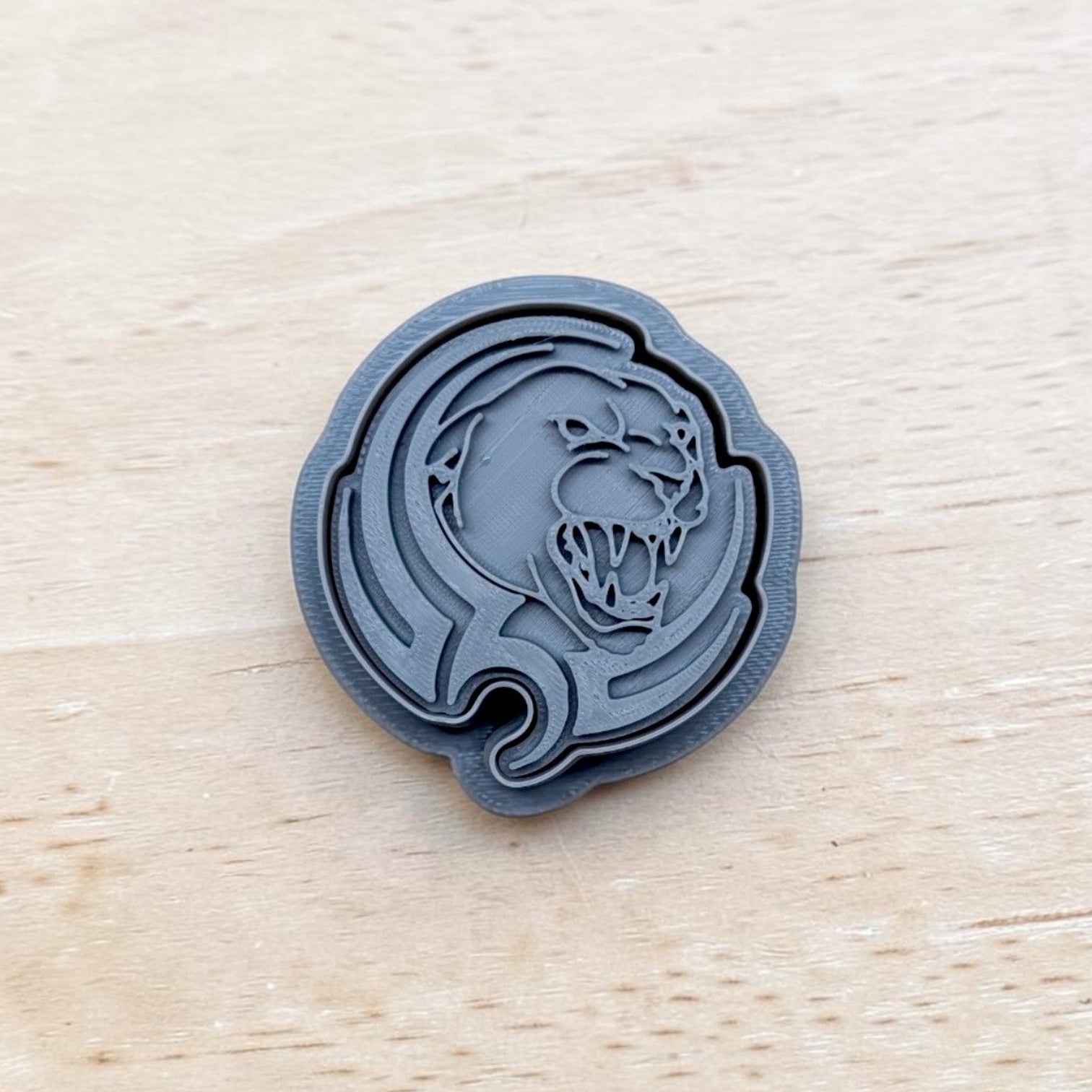 A dark gray circular stamp or embossed coin featuring a stylized panther head design, placed on a light wood surface.