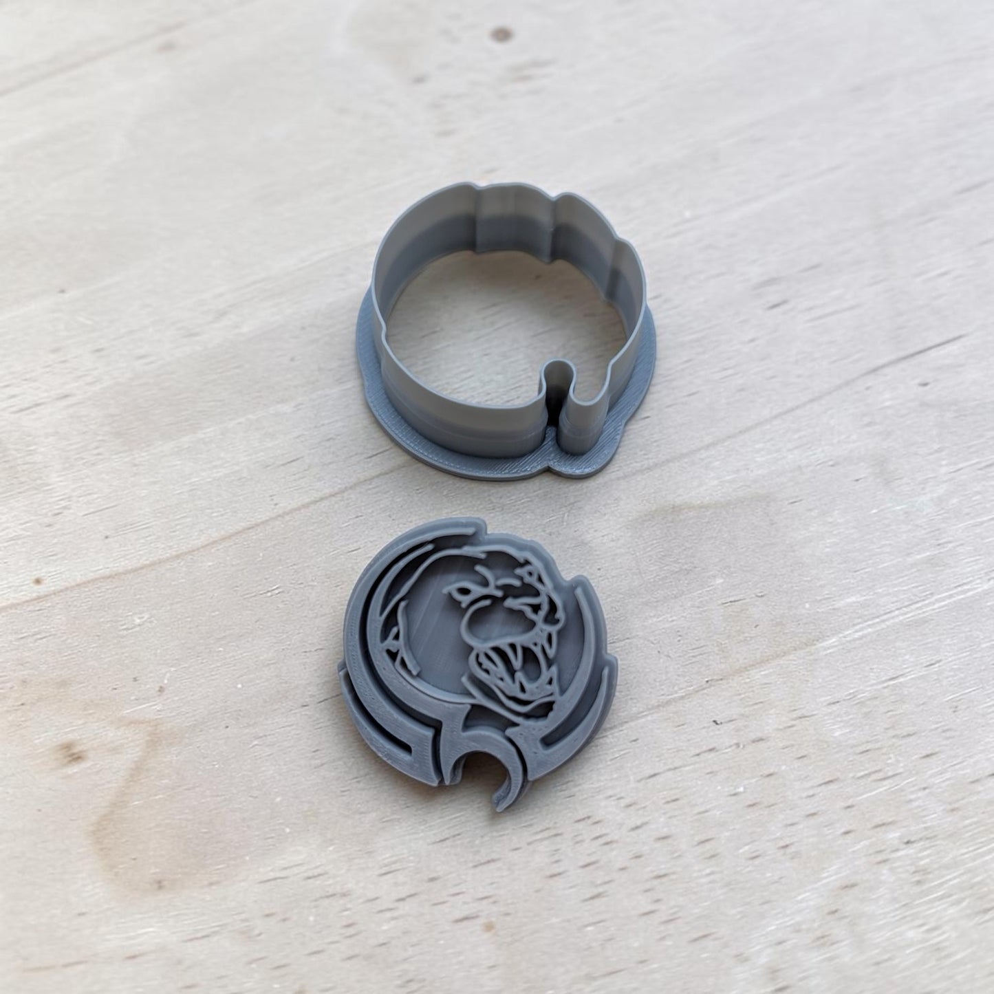 A gray plastic cookie cutter and its matching circular backing piece, featuring a detailed panther design, displayed on a light-colored wooden surface.