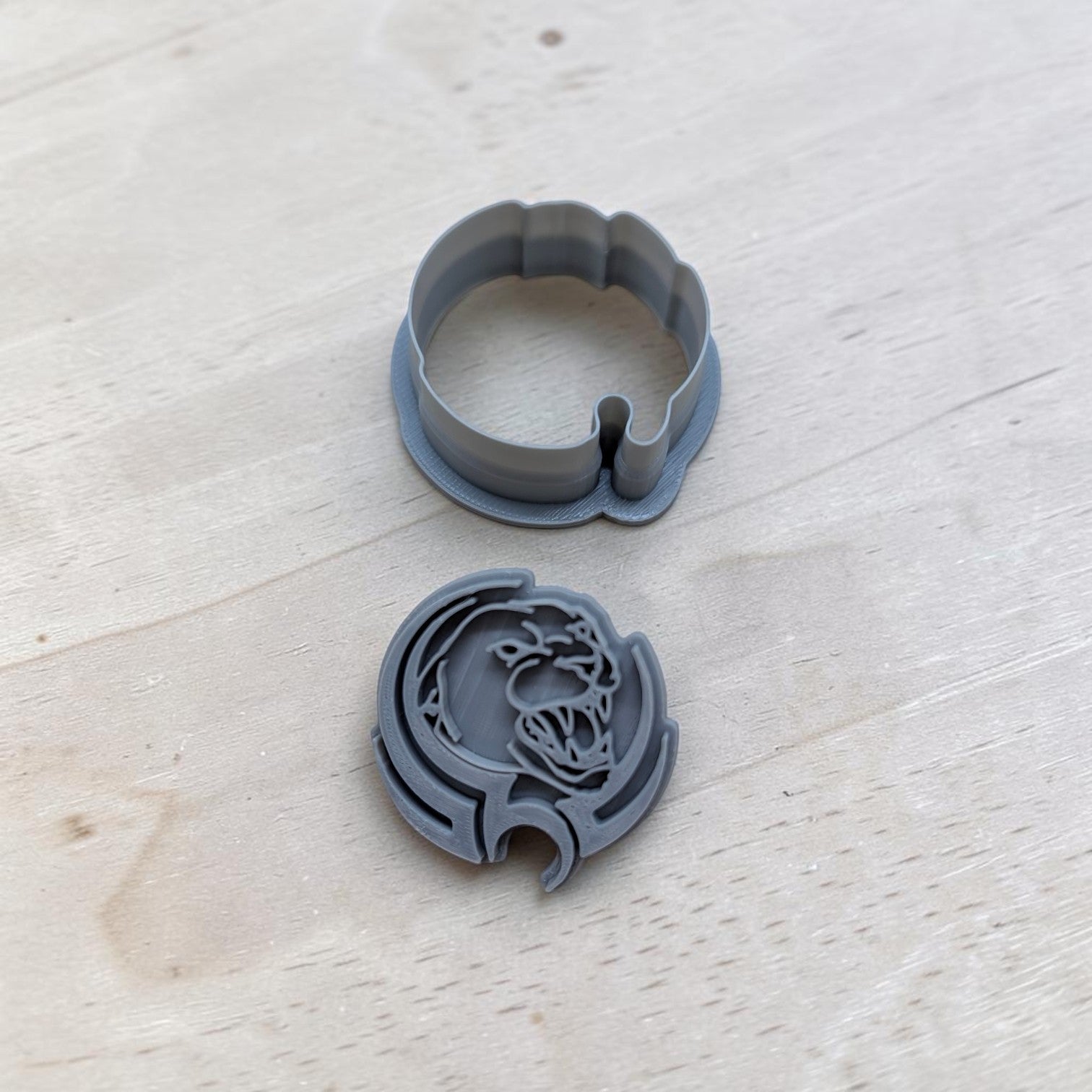 A gray plastic cookie cutter and its matching circular backing piece, featuring a detailed panther design, displayed on a light-colored wooden surface.