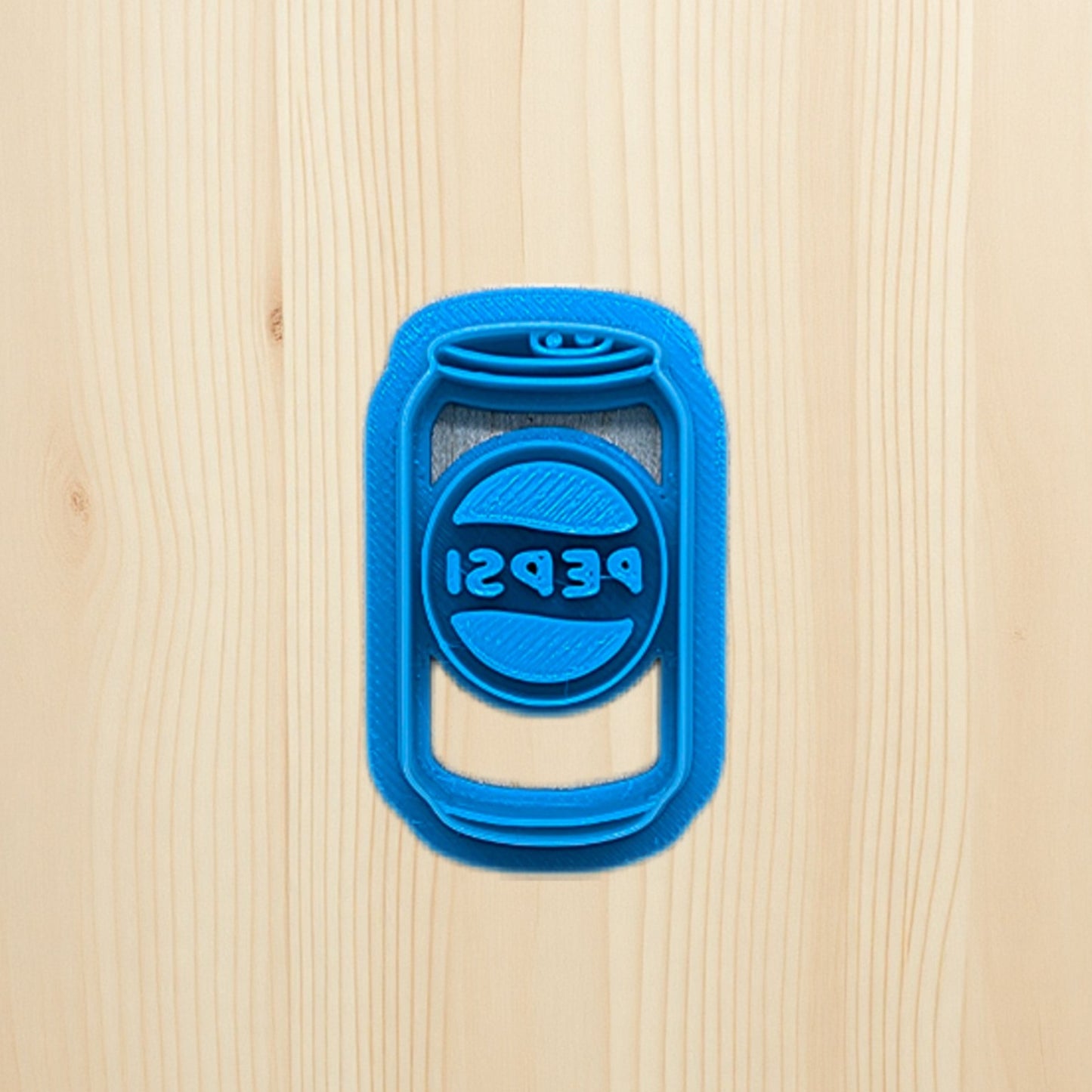 Plastic blue cookie cutter shaped like a Pepsi soda can on a wooden surface
