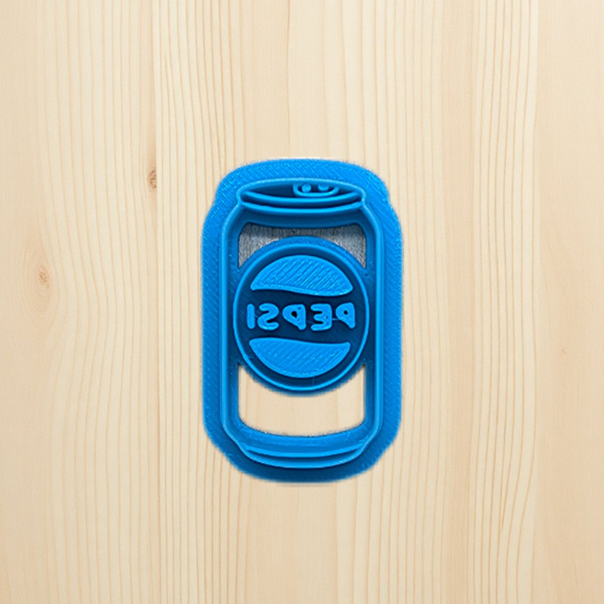Plastic blue cookie cutter shaped like a Pepsi soda can on a wooden surface