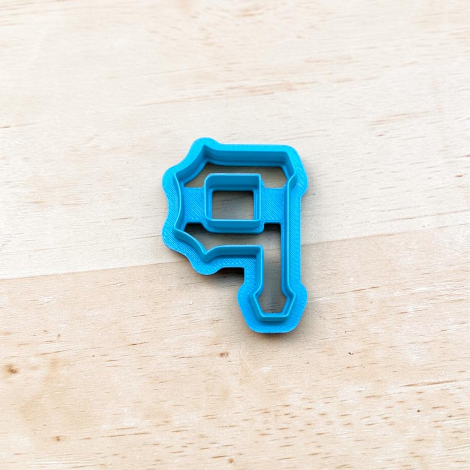 Blue cookie cutter shaped like the Pittsburg Pirates P logo on a wooden surface