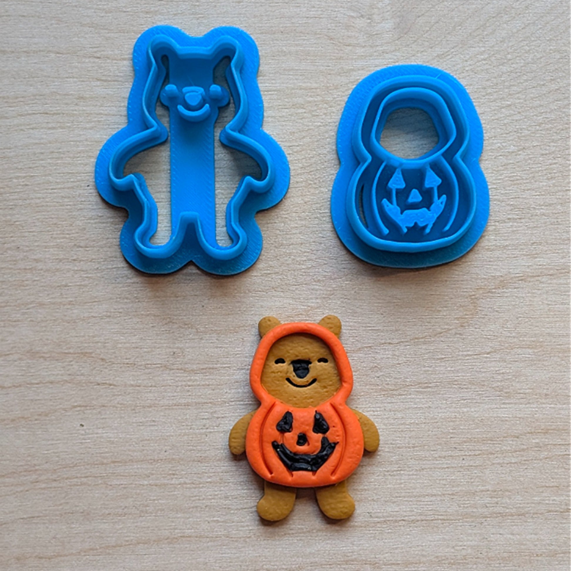 Blue bear and pumpkin cookie cutters with a Halloween-themed cookie on a wooden surface
