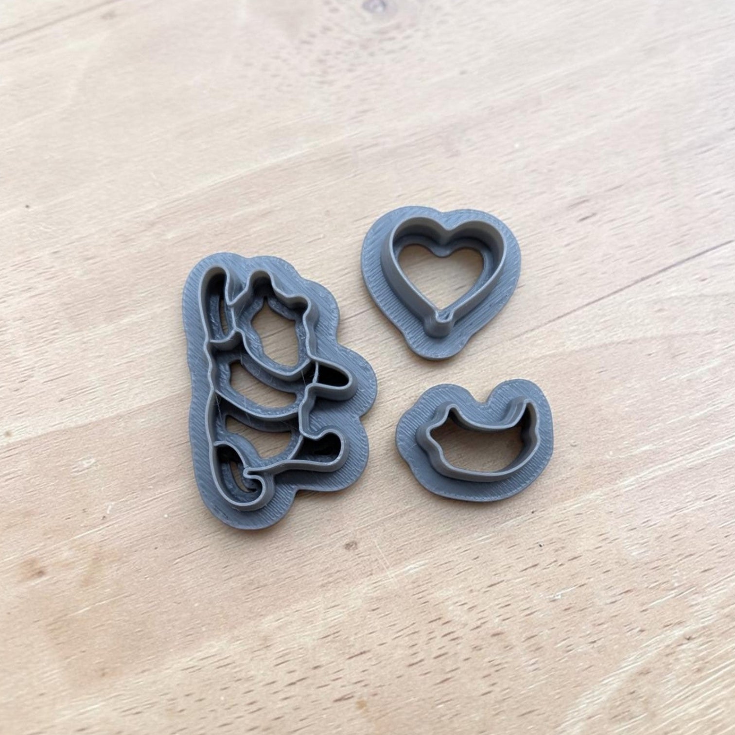 gray Pooh, shirt, and heart balloon cookie cutters on a light wooden background.