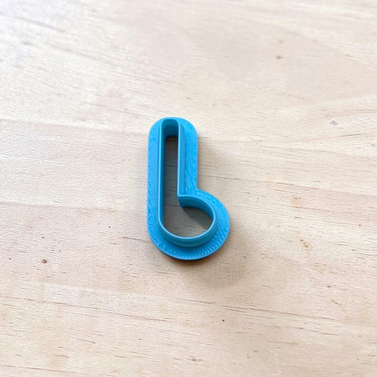 Blue 3D printed hook-shaped polymer clay cutter tool on wooden surface