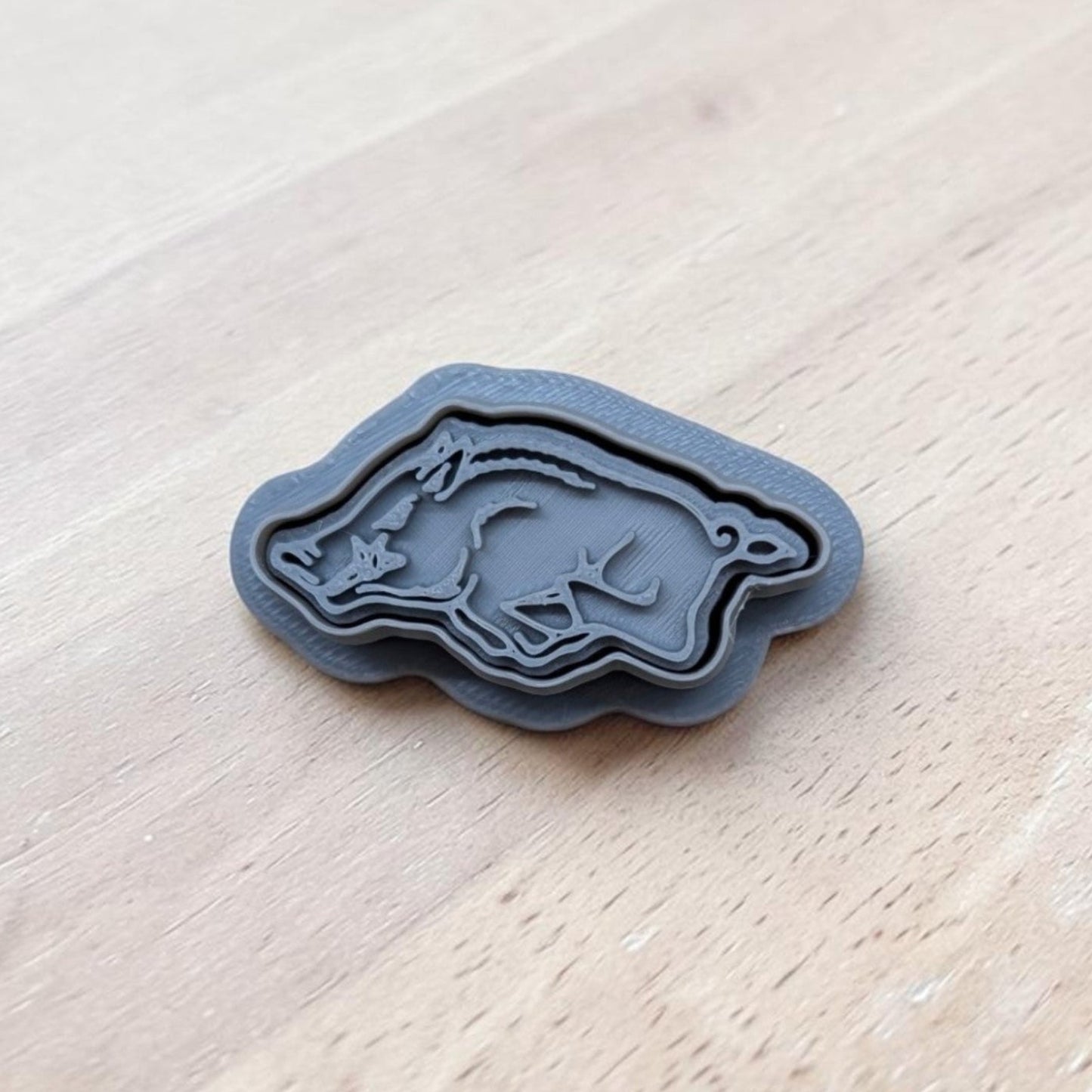 3D printed gray razorback cookie cutter and stamp set on light wood surface, ideal for cookies, fondant, clay, and pottery crafting