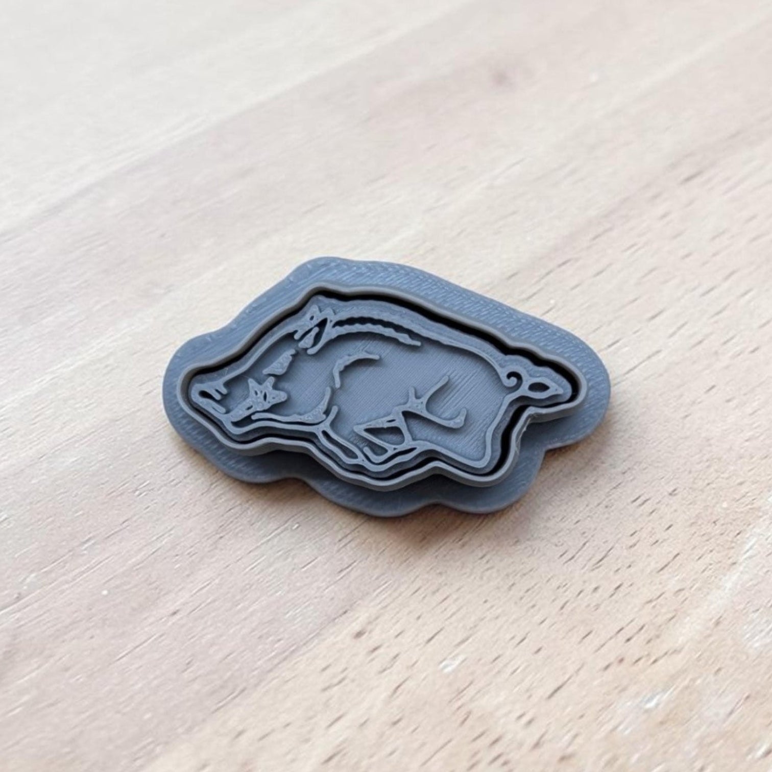 3D printed gray razorback cookie cutter and stamp set on light wood surface, ideal for cookies, fondant, clay, and pottery crafting
