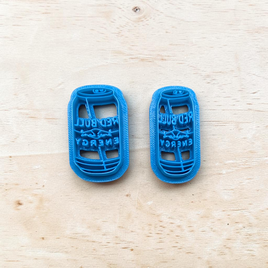 Two blue 3D-printed cookie cutters shaped like energy drink bottles on a wooden surface.