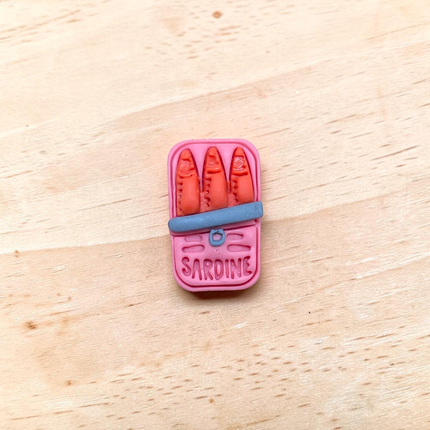 Pink sardine can-shaped container with red items on a wooden surface
