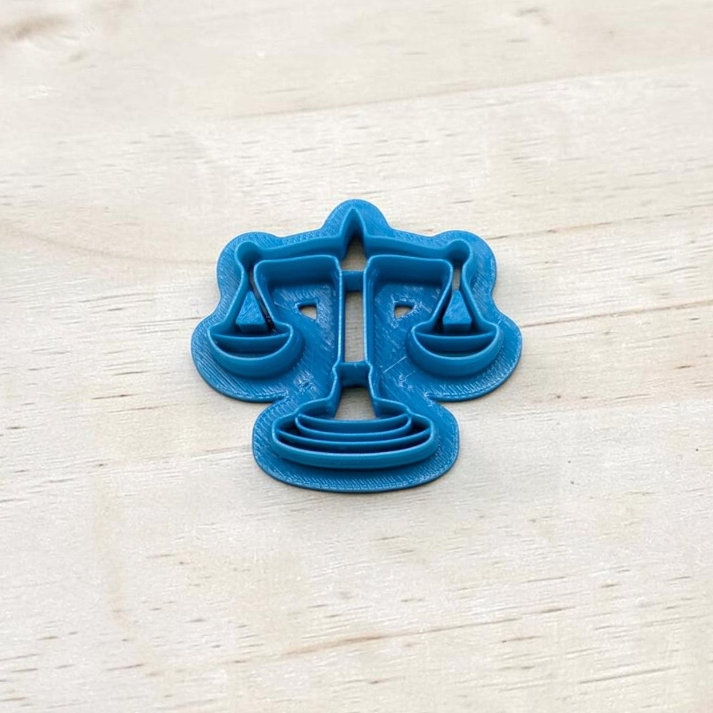 Blue cookie cutter shaped like the scales of justice symbol on a light wooden surface