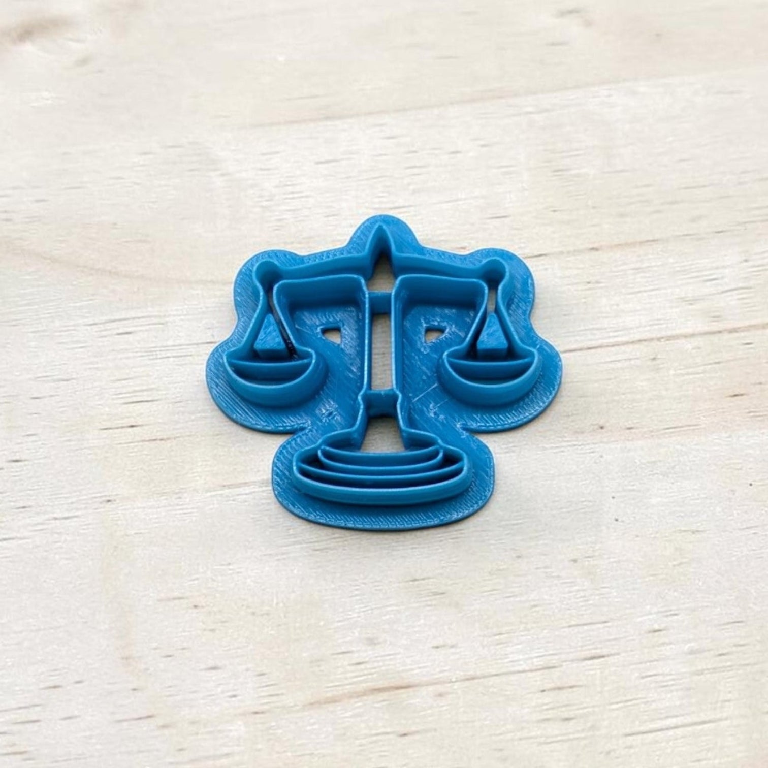 Blue cookie cutter shaped like the scales of justice symbol on a light wooden surface