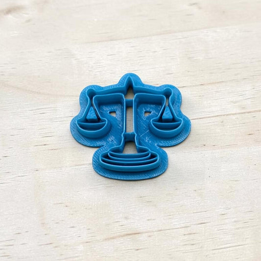 Blue cookie cutter shaped like the scales of justice symbol on a light wooden surface