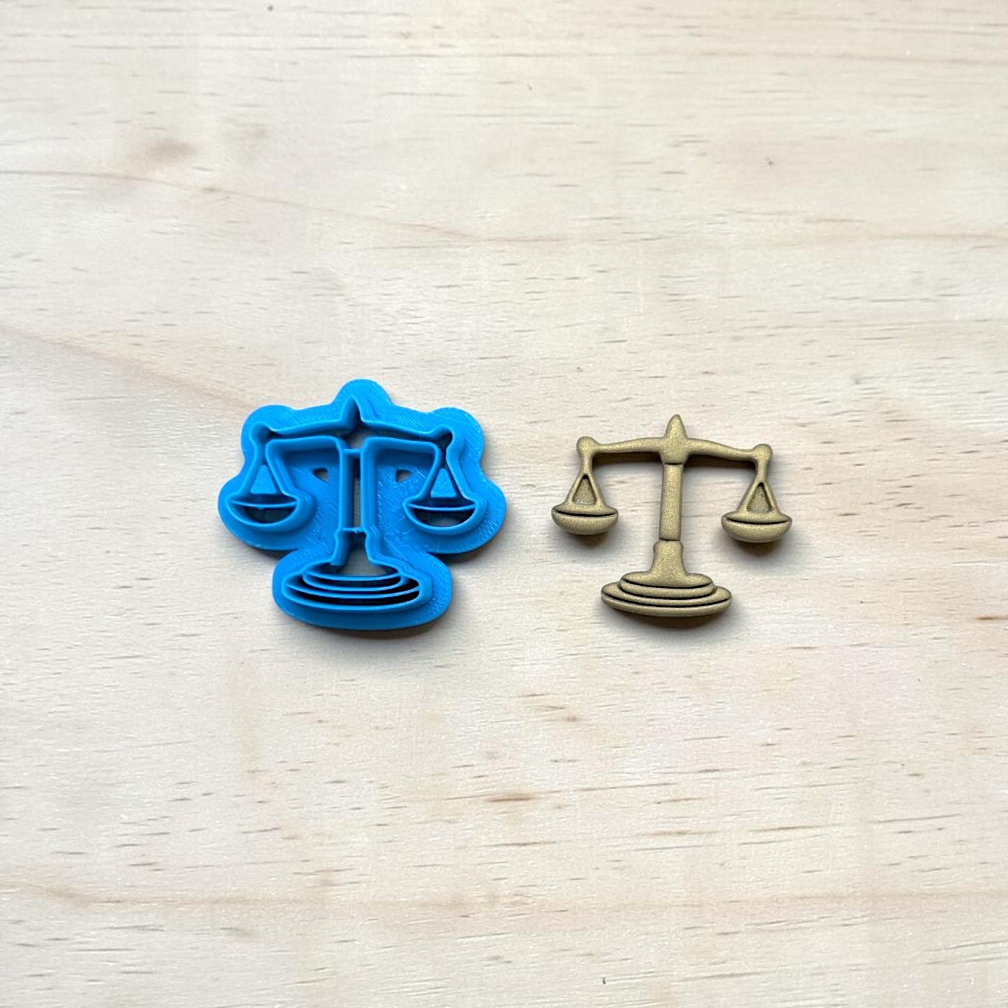 
Scales of Justice cookie cutter and matching metal emblem on light wood background for pottery, clay, fondant, and baking projects.