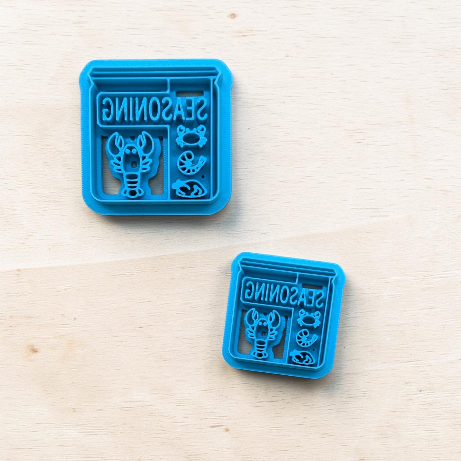 Two blue seasoning container cookie cutters on a light wooden surface