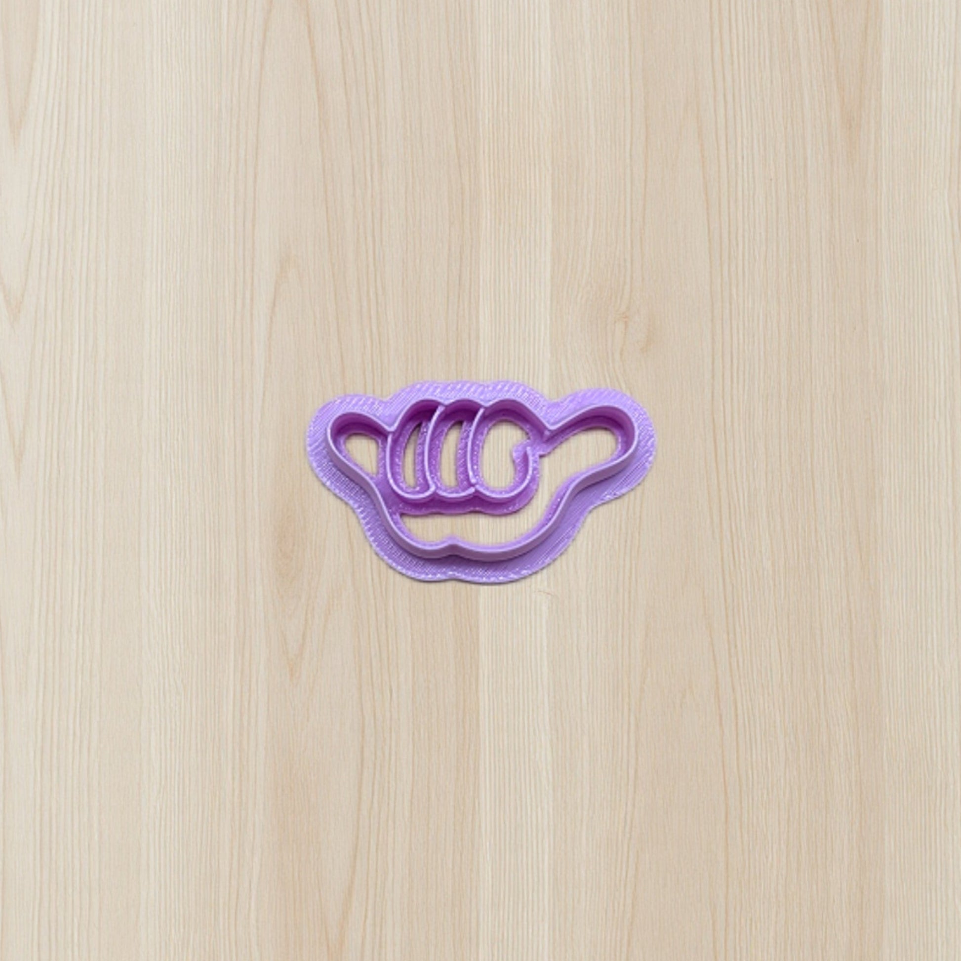 Purple cookie cutter shaped like a shaker hand gesture on a wooden surface