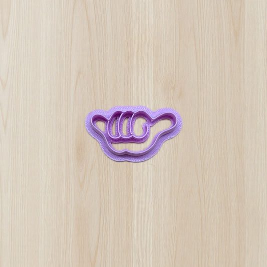 Purple cookie cutter shaped like a shaker hand gesture on a wooden surface