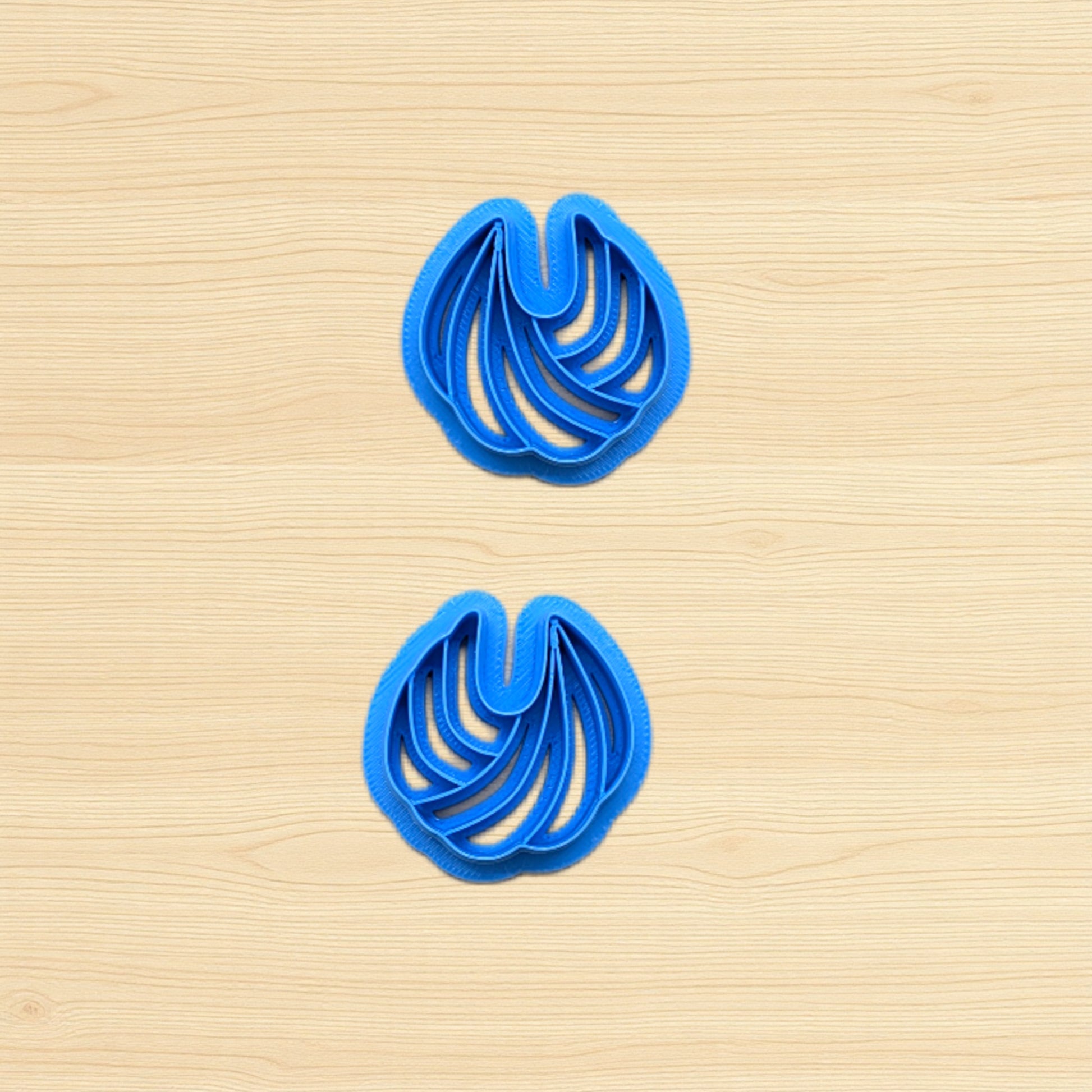 Two blue cookie cutters shaped like wavy lines on a wooden surface