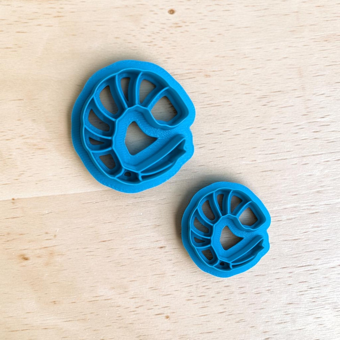 Two blue cookie cutters shaped like shrimp on a wooden surface