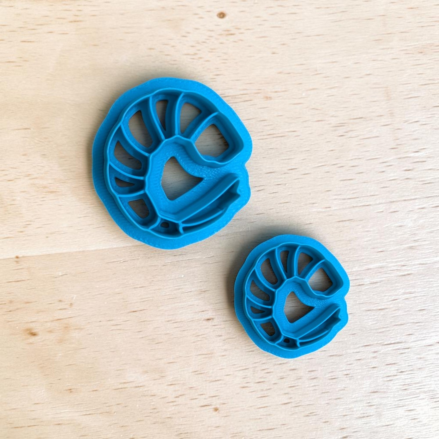 Two blue cookie cutters shaped like shrimp on a wooden surface
