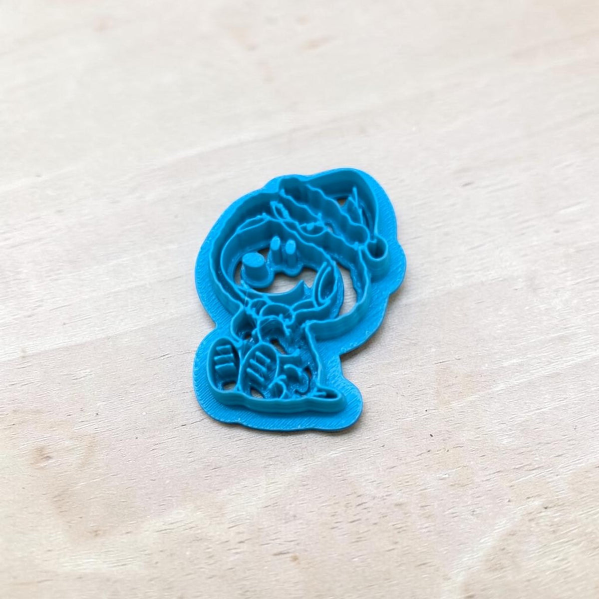 Blue 3D-printed Snoopy in Grinch Costume Cookie Cutter with detailed Christmas character design, photographed on a light wood surface. Ideal for holiday sugar cookies, polymer clay earrings, fondant decorations, pottery, and ceramic crafts.
