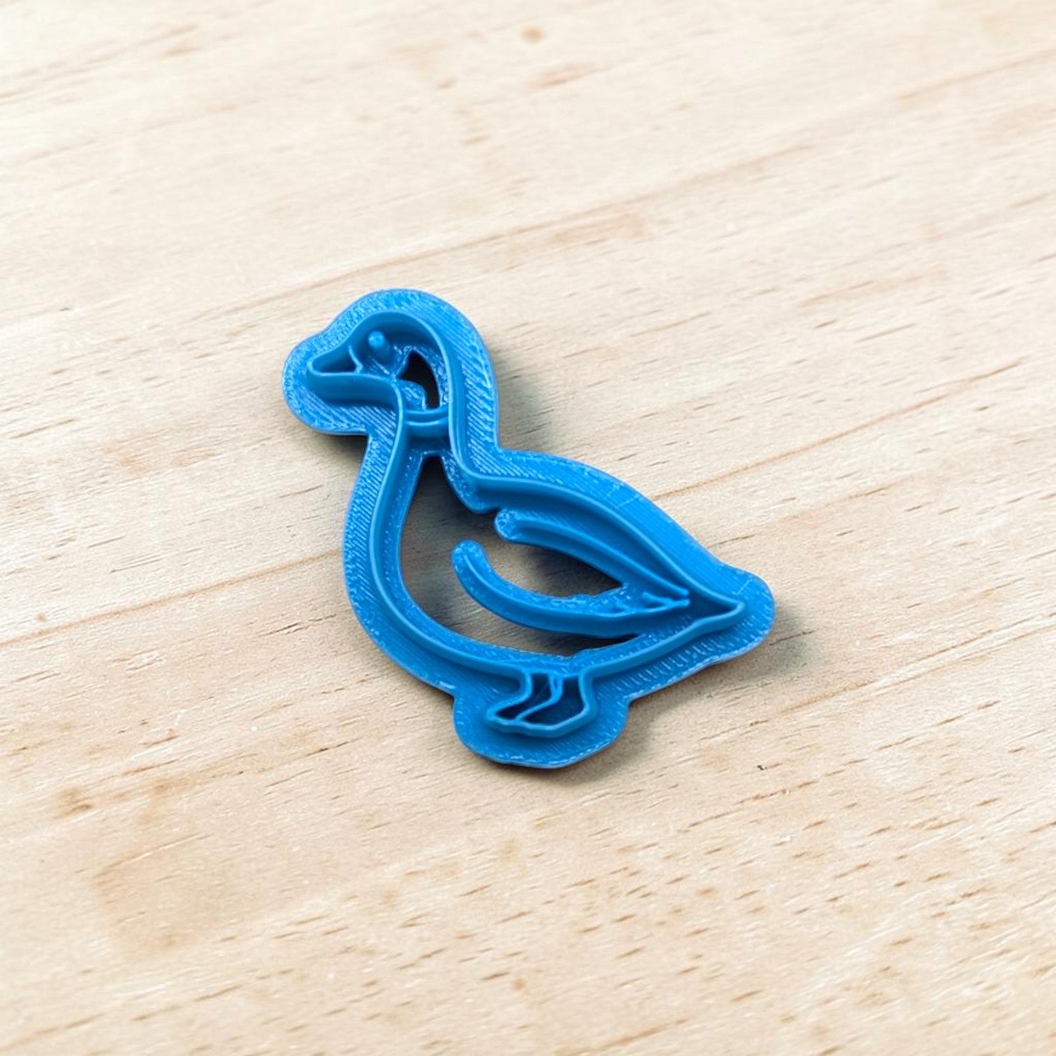 Blue cookie cutter shaped like a duck on a wooden surface