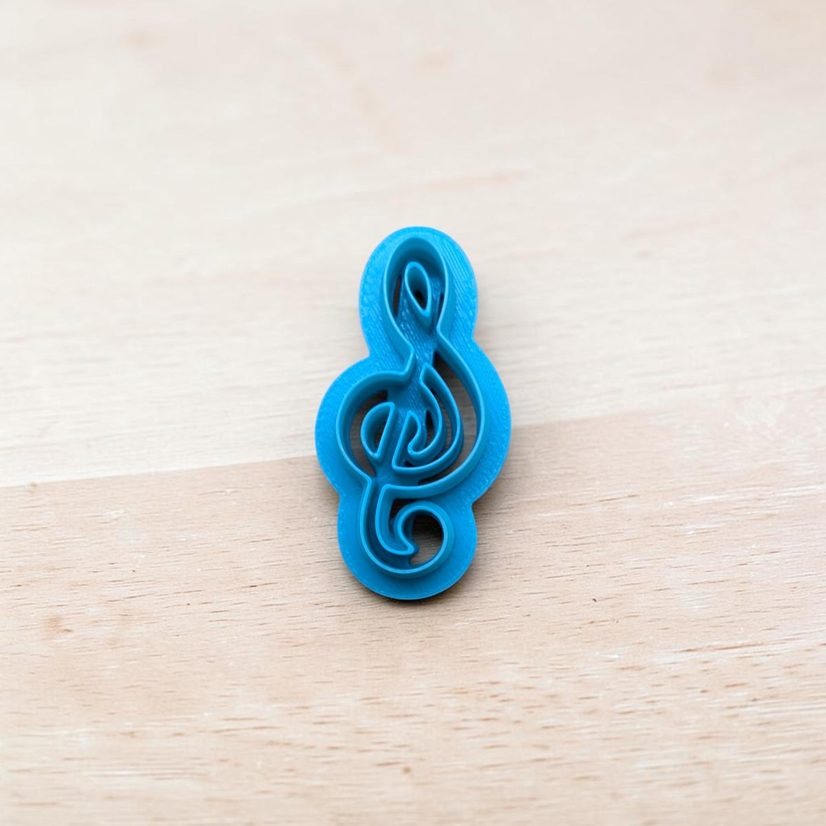 Blue 3D‑printed treble clef cookie cutter on light wood background — polymer clay and fondant tool by Truley Unique.