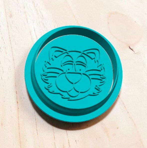 Turquoise round tiger mascot cookie cutter and embosser with cartoon face design on wooden background