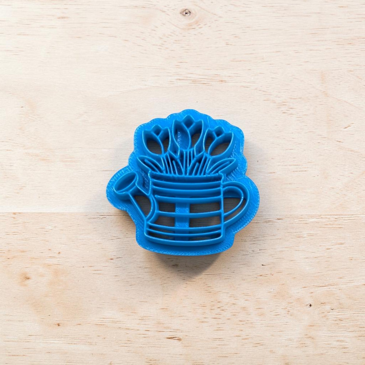 Blue cookie cutter shaped like a watering can with tulips inside on a wooden surface