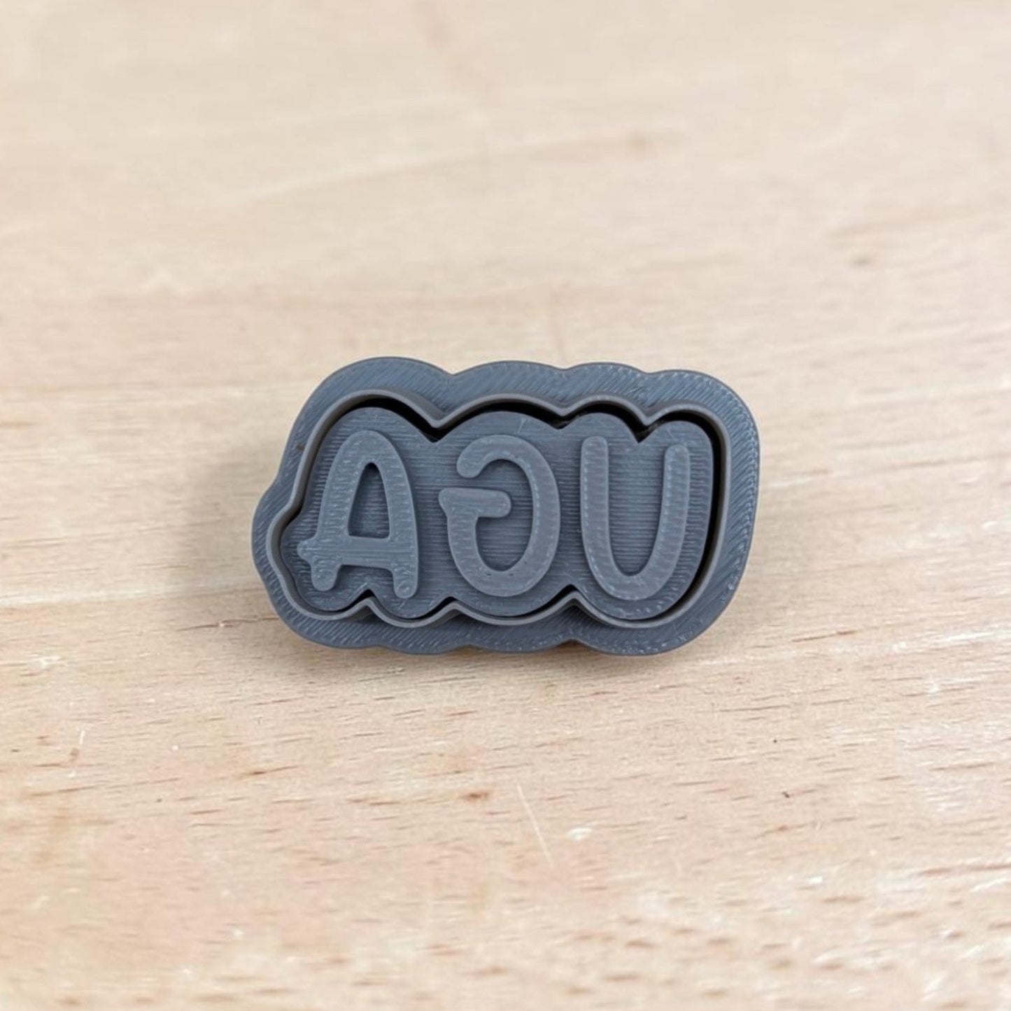 3D printed UGA stamp with mirrored lettering on light wood surface, ideal for cookie or clay embossing