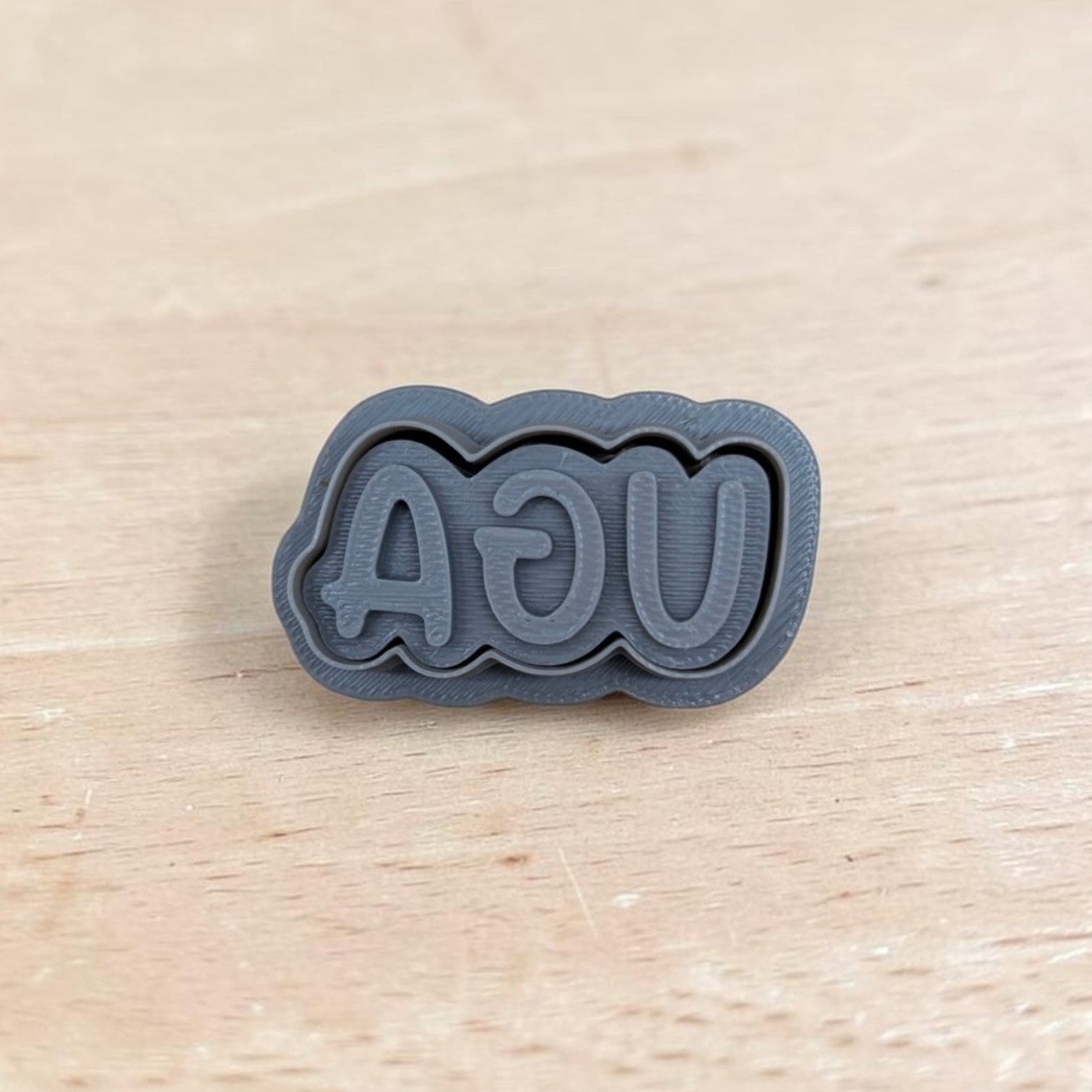 3D printed UGA stamp with mirrored lettering on light wood surface, ideal for cookie or clay embossing