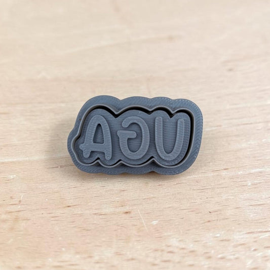 3D printed UGA stamp with mirrored lettering on light wood surface, ideal for cookie or clay embossing