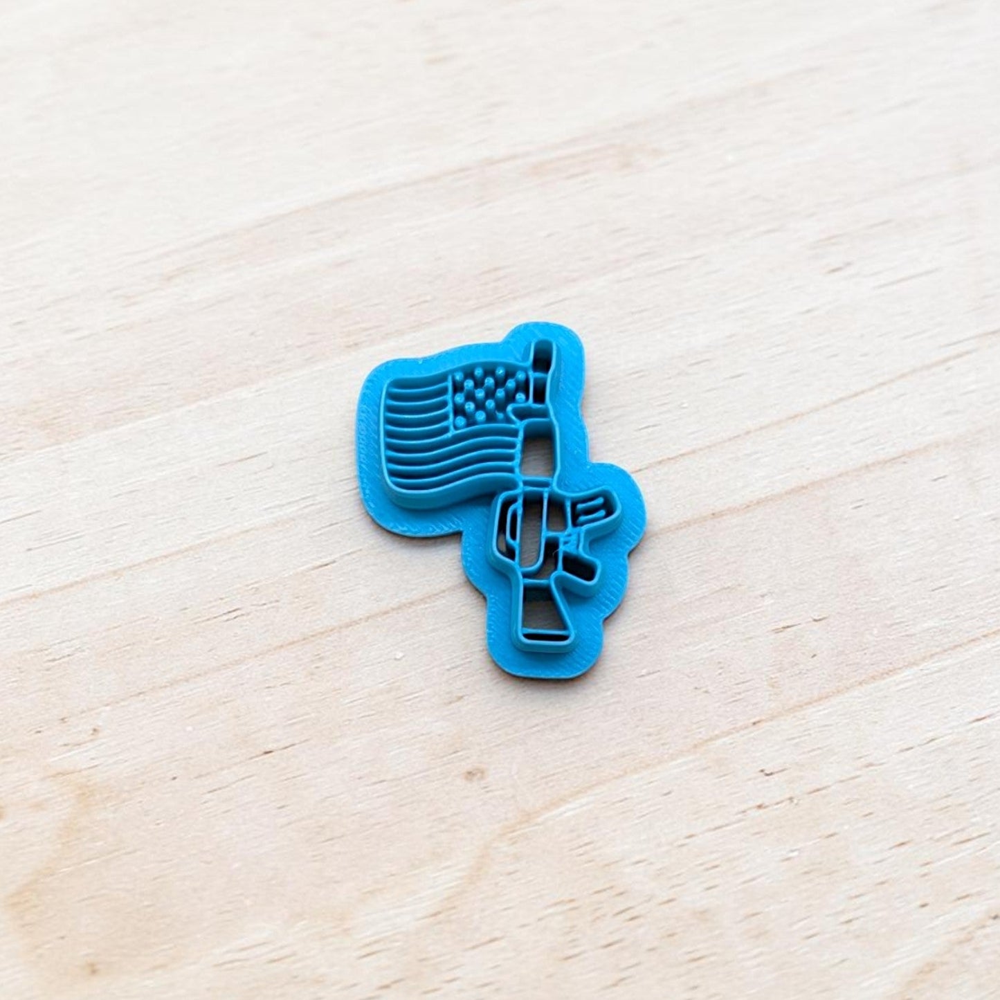 Blue cookie cutter shaped like a USA flag attached to a rifle on a light wooden surface