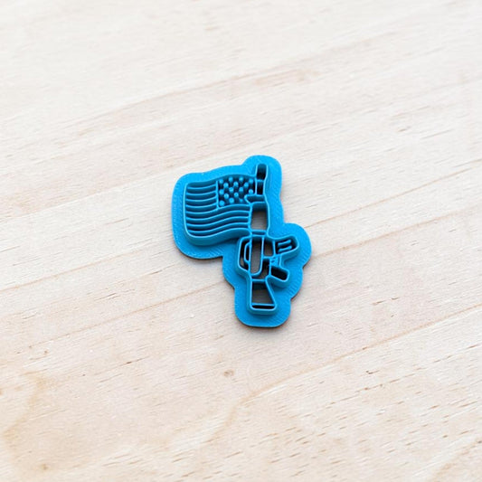 Blue cookie cutter shaped like a USA flag attached to a rifle on a light wooden surface