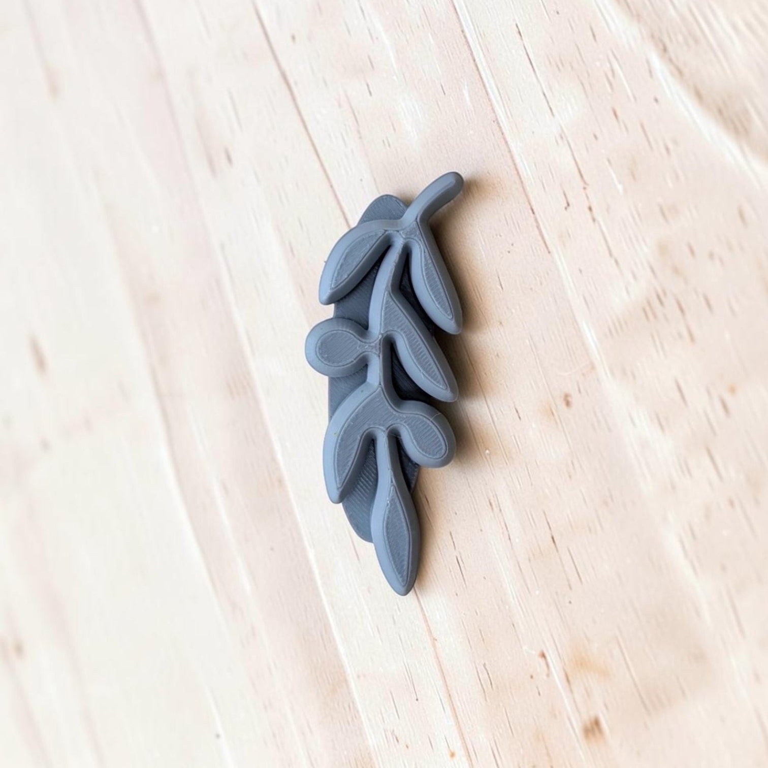 A small gray decorative branch or leaf-shaped stamp resting on a light wood surface.