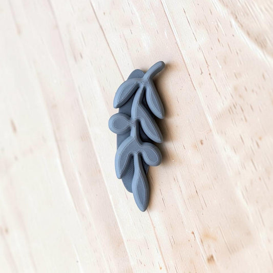 A small gray decorative branch or leaf-shaped stamp resting on a light wood surface.