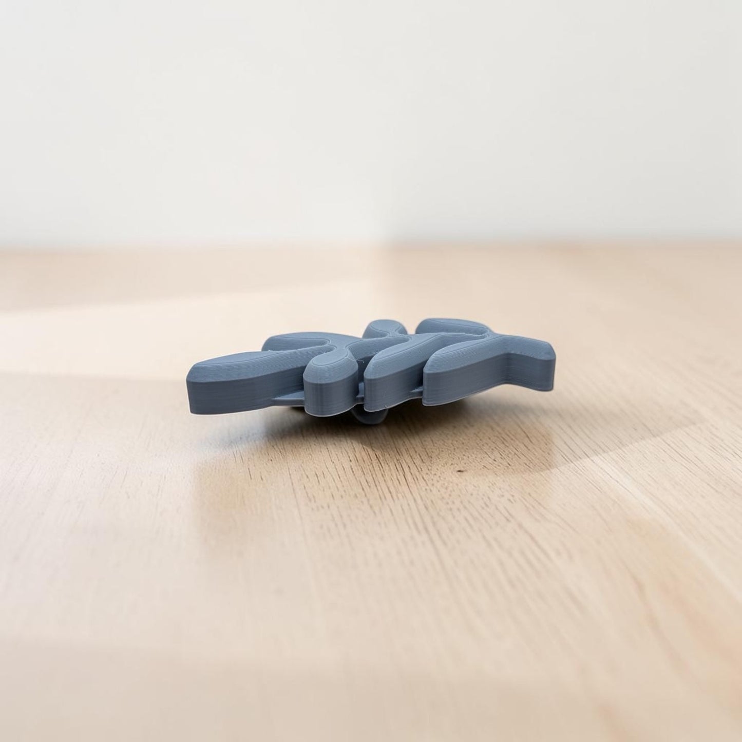A small gray plastic clip or connector with a ribbed, ergonomic design, resting on a light wood surface against a neutral off-white background.