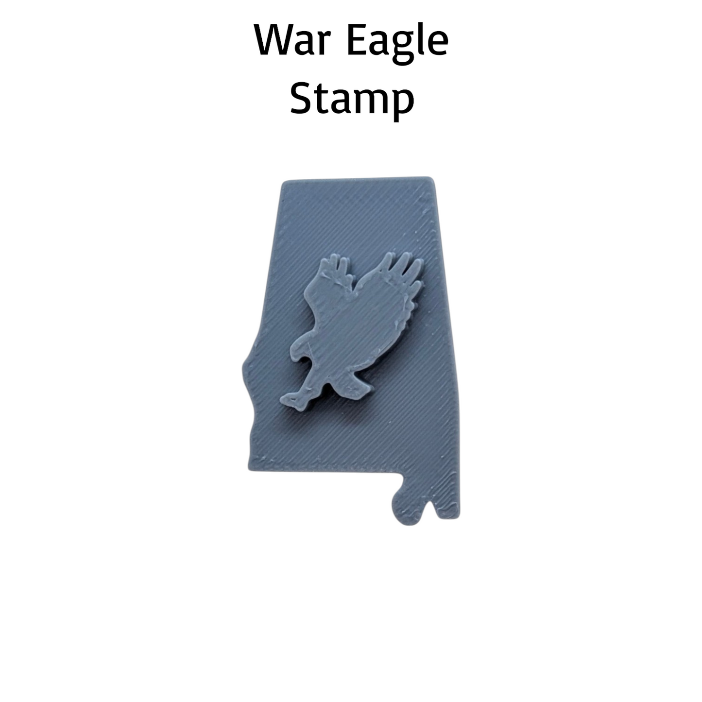 A gray 3D-printed stamp shaped like the state of Alabama, featuring a raised war eagle design in the center. The text 'War Eagle Stamp' is printed above the product on a solid white background.