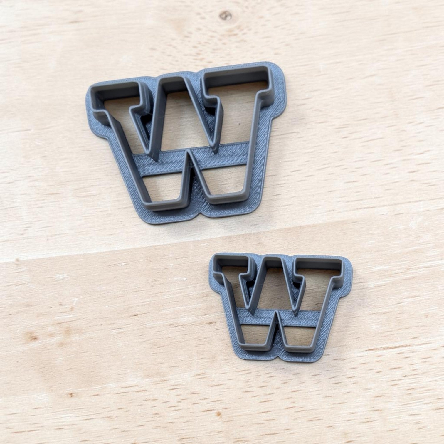 Two dark gray letter 'W' cookie cutters on a light wood background.