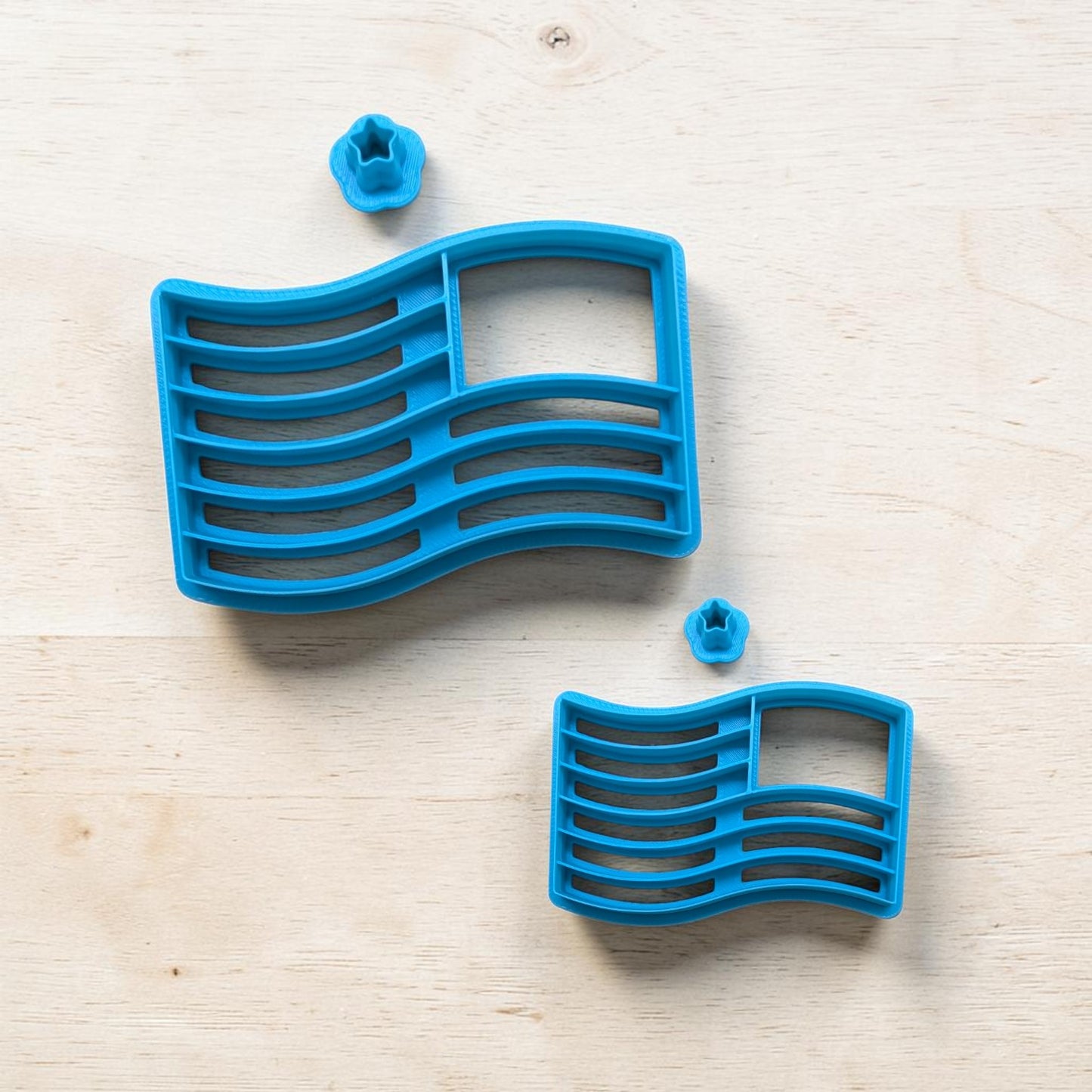 Blue cookie cutter shaped like a wavy flag on a light wooden surface