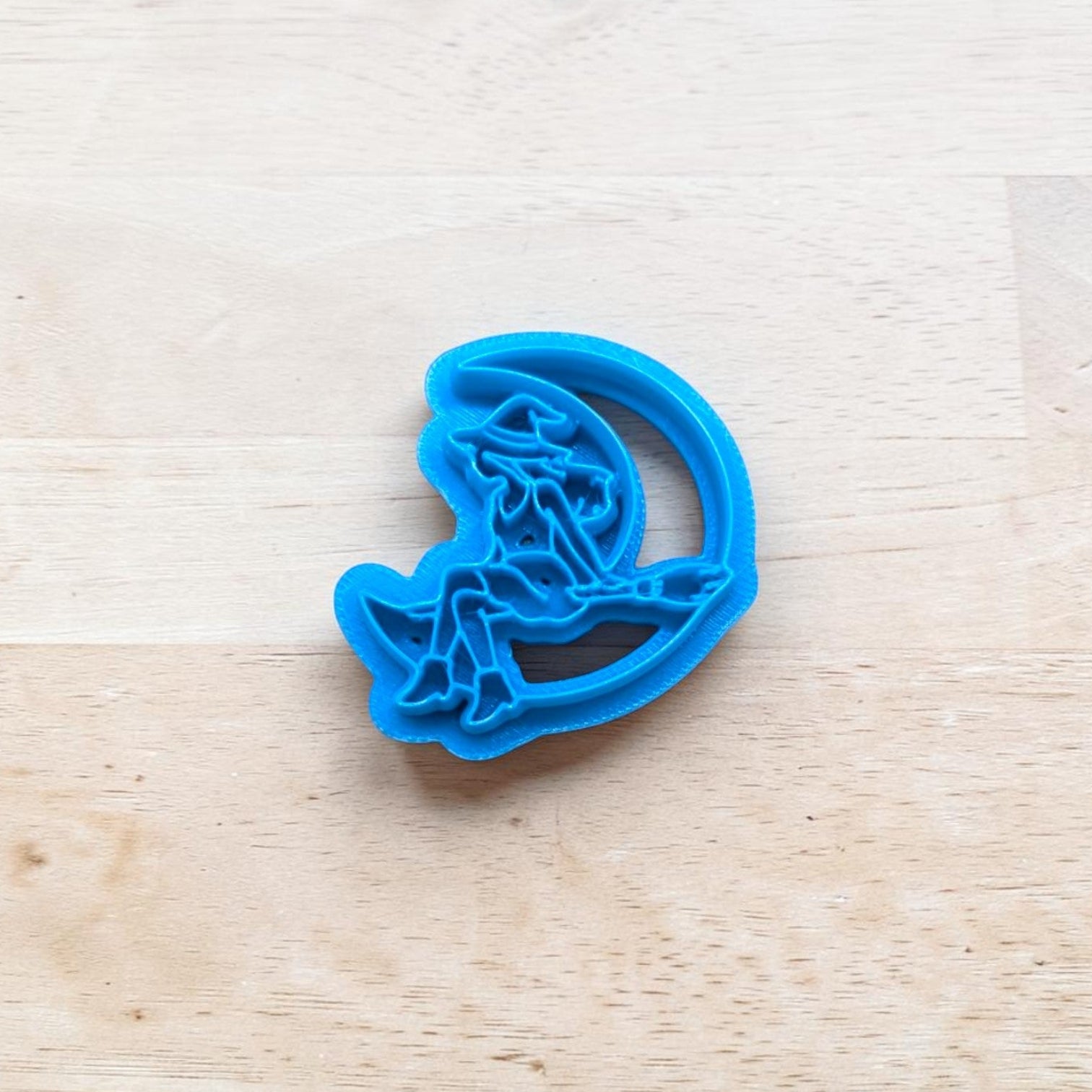 Blue cookie cutter with a witch on the moon design on a wooden surface