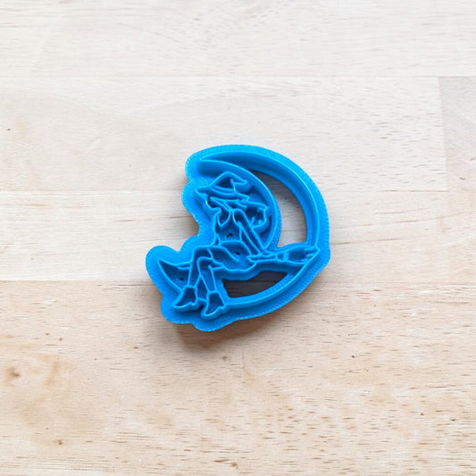 Blue cookie cutter with a witch on the moon design on a wooden surface