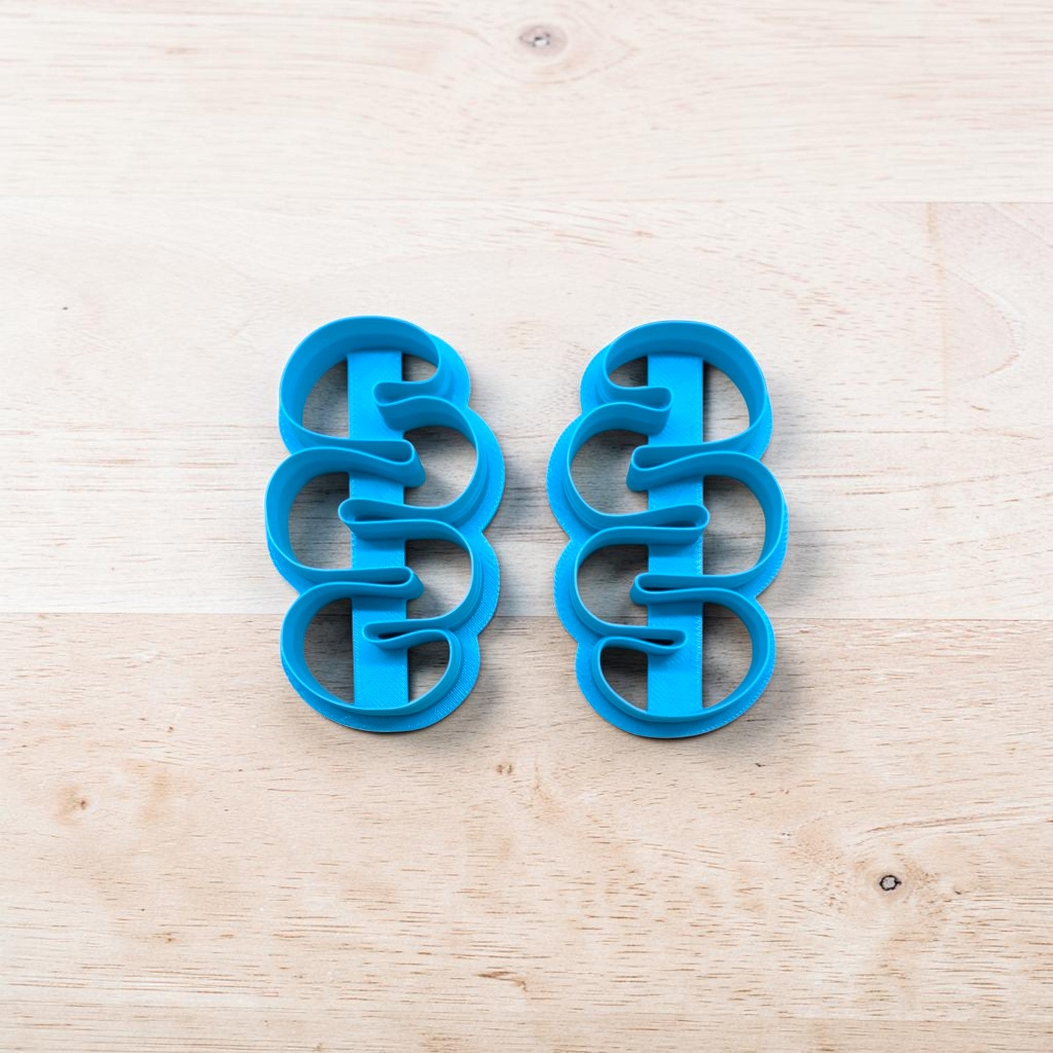 Two blue cookie cutters shaped like snakes on a light wooden surface.