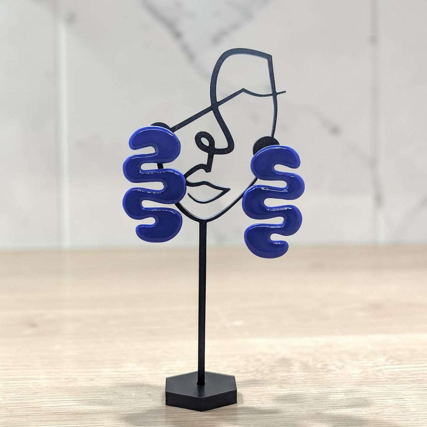 Blue spiral earrings on a black stand against a light background