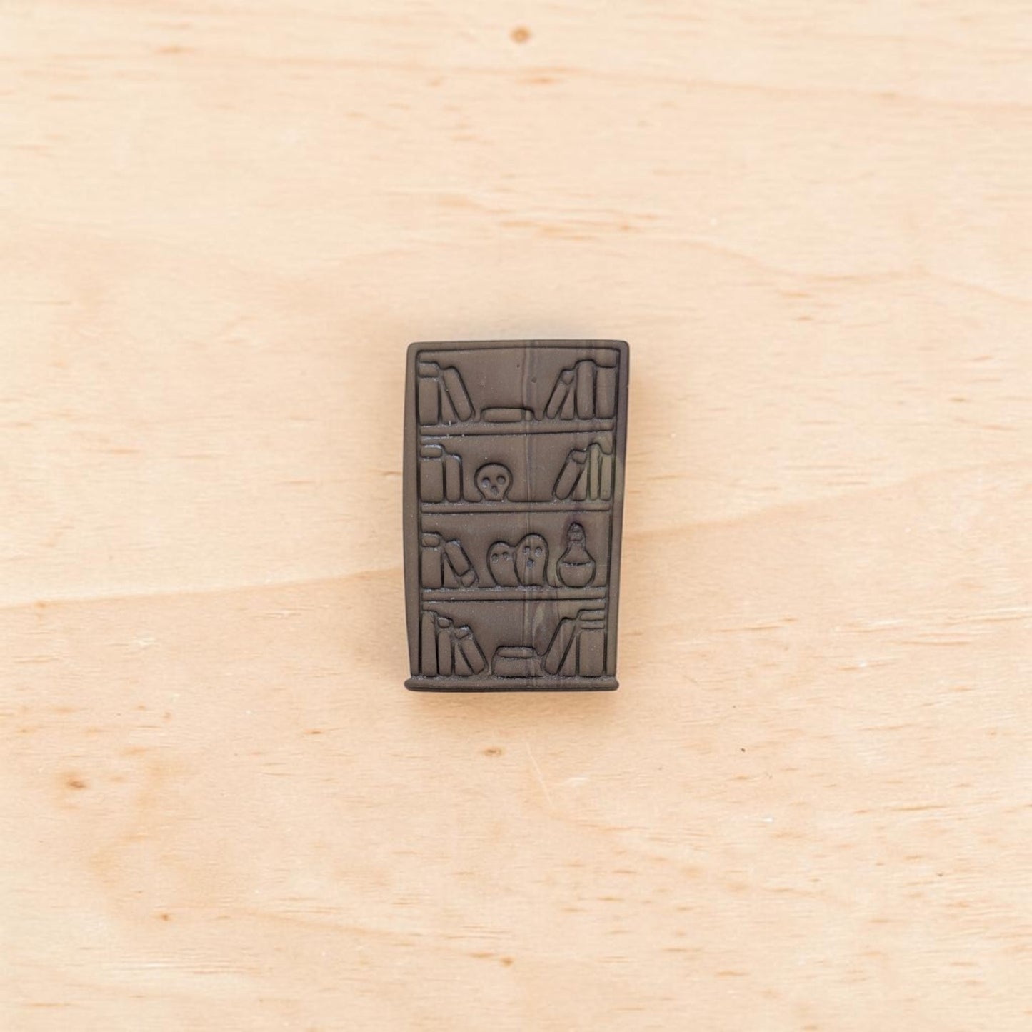 Embosser impression of haunted bookshelf cutter – detailed polymer clay stamp showing books, skull, and potion bottle design.