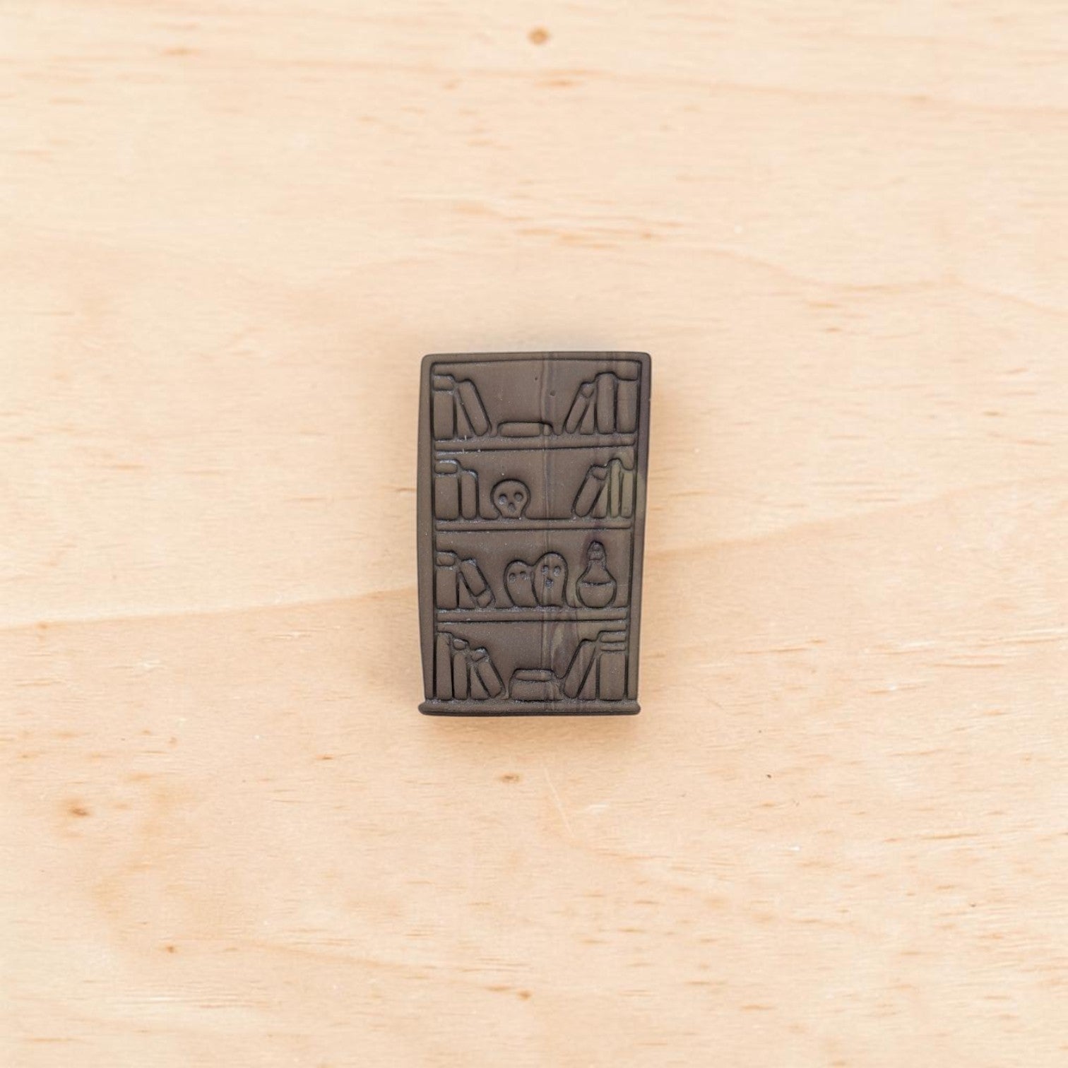 Embosser impression of haunted bookshelf cutter – detailed polymer clay stamp showing books, skull, and potion bottle design.