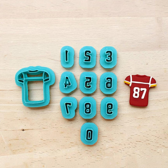 turquoise jersey-shaped cookie cutter set with number cutters and decorated red football jersey cookie featuring white number 87 on light wood background